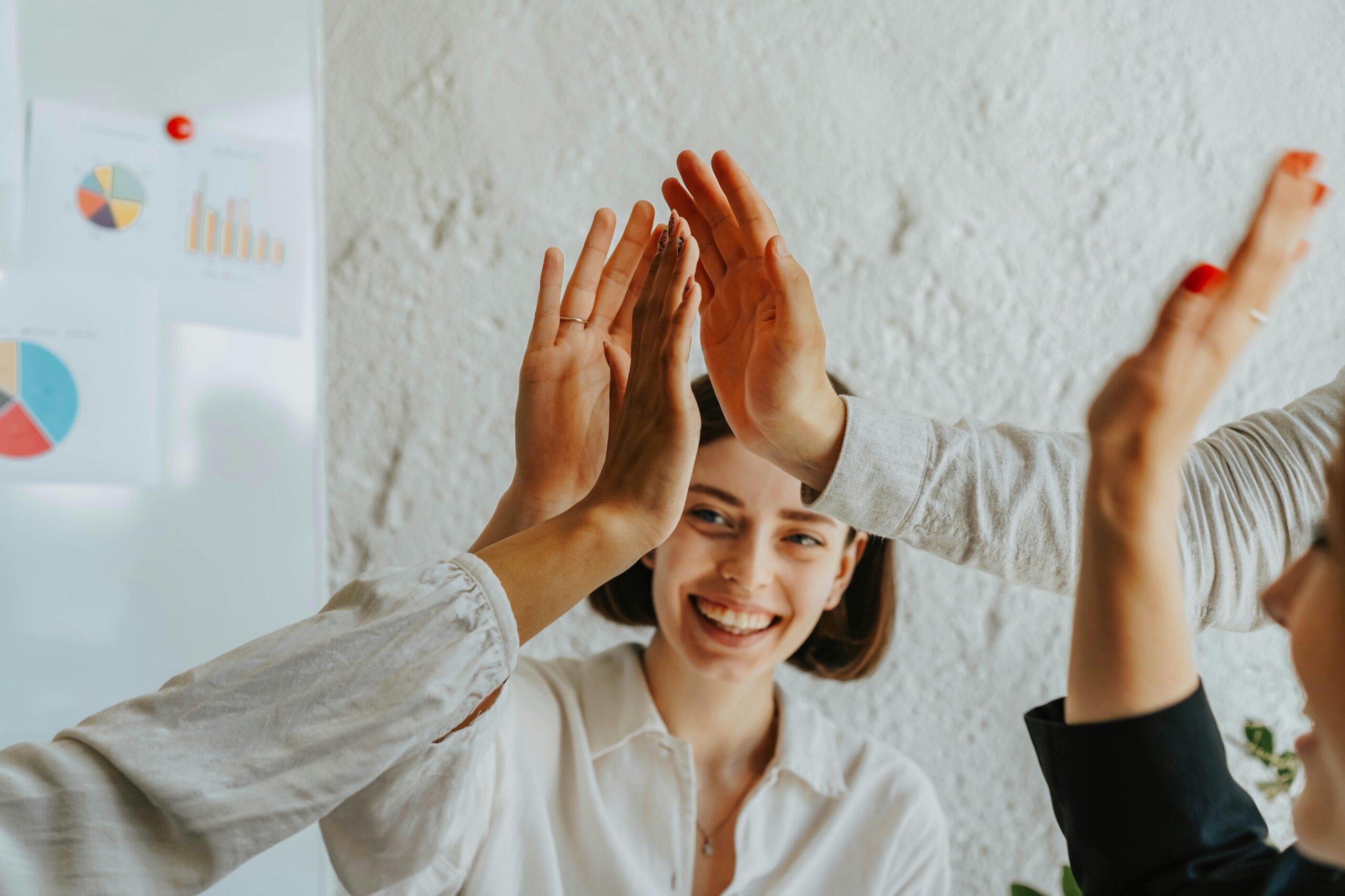 Group of smiling adults engaging in a teamwork high five celebration in an office setting.